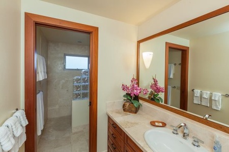 - Stylish bathroom with wood vanity and marble countertop for elegance   - Large framed mirror brightens the space alongside warm ambient lighting   - Doorway leads to a walk in shower with natural light from glass block windows