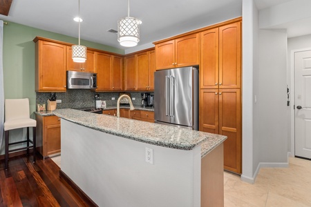 - Kitchen with granite countertops, stainless steel refrigerator, and warm wood cabinetry - Pendant lights illuminate the breakfast bar for casual dining - Functional design combines style and convenience for guests