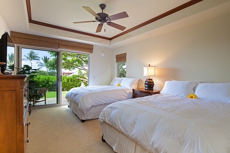 - Bright guest bedroom with two queen beds dressed in crisp white linens   - Ceiling fan and sliding doors open to a private patio with tropical views   - Warm wood accents and soft lighting create a peaceful retreat for guests