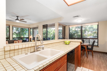 Your open-concept kitchen flows seamlessly into the dining area, surrounded by tropical garden views through expansive windows.
