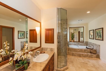 - Stylish bathroom featuring marble countertops and warm wood cabinetry - Glass shower enclosure pairs with a deep soaking tub for complete comfort - Elegant lighting and floral accents create a serene, spa inspired escape
