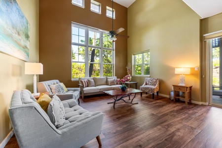 Unwind in this sunlit living space with soaring ceilings, elegant wood floors, and plush seating. Large windows frame garden views, while a ceiling fan keeps you comfortable as you relax.