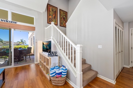 - White staircase adds charm and leads to peaceful upstairs bedrooms and baths - Below, a cube shelf holds beach towels and a flatscreen TV for entertainment - Tropical wall art and wicker basket touches complete the welcoming entry