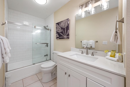 - Bright full bathroom features a white vanity, updated lighting, and framed art - Glass enclosed tub and shower combo offers both style and functionality - Subtle tile, chrome finishes, and thoughtful touches elevate the space