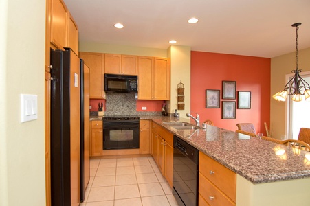 - Kitchen with granite countertops, wood cabinetry, and black appliances - Double sink overlooks the dining area for convenient meal prep - Plenty of storage and open layout make cooking a breeze