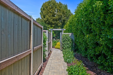 A paved pathway leads through lush landscaping to the property entrance, surrounded by mature trees and manicured gardens.