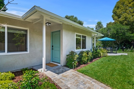 Modern property nestled among mature trees with charming turquoise entrance and landscaped grounds featuring peaceful garden areas.