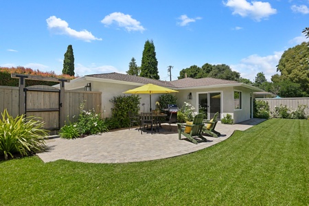 Single-story rental home featuring manicured lawn, paved patio, and mature landscaping under clear blue skies.