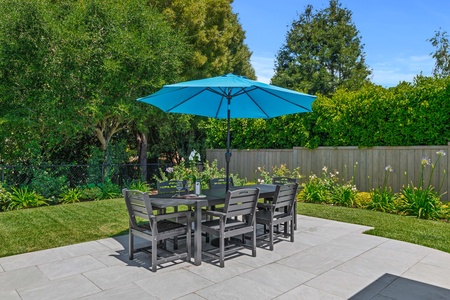 Gather around your private dining table in this sun-dappled garden oasis, where meals become memorable under the bright blue umbrella.