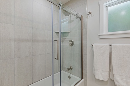 Step into your sleek bathroom featuring a spacious glass-enclosed shower with rain head and modern fixtures, complete with fresh towels.