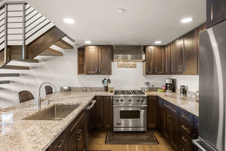 A modern kitchen features dark wood cabinets, stainless steel appliances, granite countertops, and a spiral staircase leading upstairs.