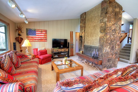 Cozy living room with striped sofas, a red armchair, an American flag on the wall, a TV, a stone fireplace, and rustic decorations.