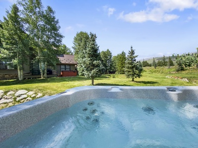 View from a hot tub looking over a grassy yard with several trees and a house in the background under a partly cloudy sky.