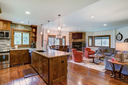 A modern open-concept living space featuring a kitchen with wooden cabinets and an island, a dining area with a chandelier, and a cozy living room with a fireplace and comfortable seating.