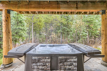 A covered outdoor hot tub with bubbling water, surrounded by wooden beams and overlooking a forested area.