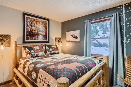 A cozy bedroom with a rustic wooden bed, forest-themed bedding, wall art, and a window showing a snowy outdoor scene.