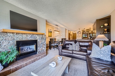 Cozy up in this inviting living room with plush leather seating, a warm stone fireplace, and stunning mountain views right from your private balcony.