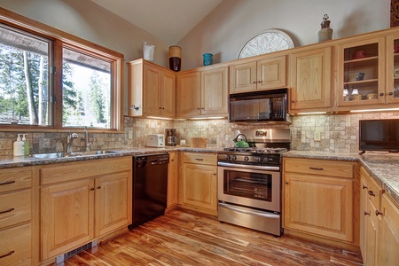 A kitchen with wooden cabinets, stainless steel appliances, and a tile backsplash. Large window provides natural light, and countertops are clutter-free with minimal accessories.