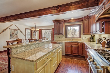 Spacious kitchen with wooden cabinets, granite countertops, an island, a gas stove, and a dining area in the background. Large window over the sink provides natural light.