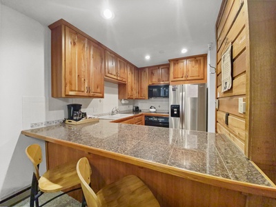 A kitchen with wooden cabinets, granite countertops, stainless steel appliances, and two wooden stools at a counter.