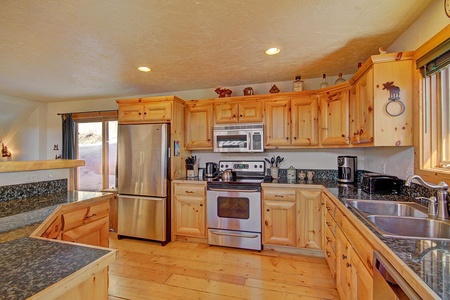 A modern kitchen with stainless steel appliances, light wooden cabinetry, granite countertops, a double sink, and hardwood floors.