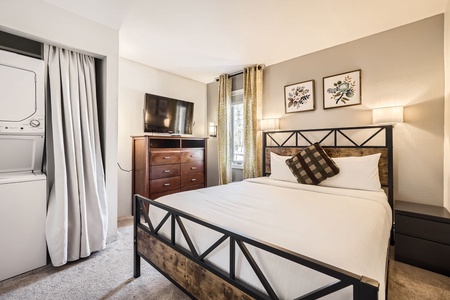 Bedroom with a dresser and Tv on top with a washer and dryer to the left of it