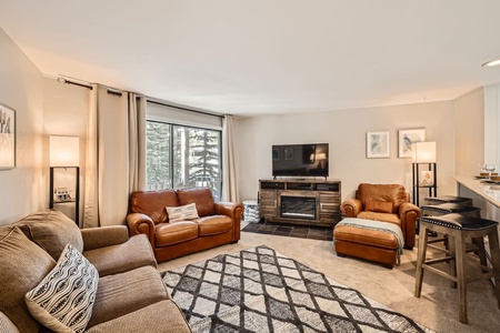 A living room with 2 sofas and a chair with a fireplace and TV on top