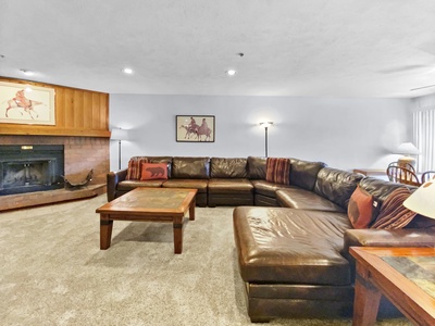 A spacious living room features a large brown leather sectional sofa, a wooden coffee table, a fireplace, and framed horse-themed artwork on the walls.