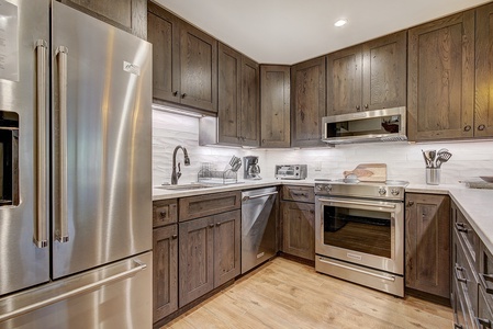 A modern kitchen with stainless steel appliances, dark wood cabinets, a double-door refrigerator, an oven, a microwave, countertop accessories, and a white tile backsplash.