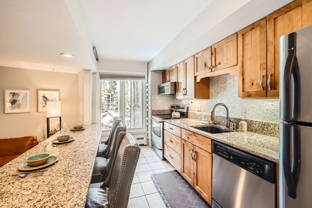 A kitchen with wooden cabinets, granite countertops, stainless steel appliances and seating area