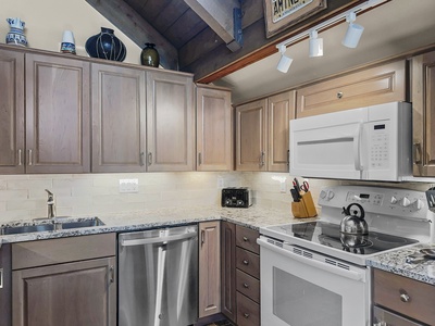 A modern kitchen with wooden cabinets, granite countertops, and stainless steel appliances. The setup includes a sink, dishwasher, stove, microwave, and various kitchen utensils. A sign reads "America" above.