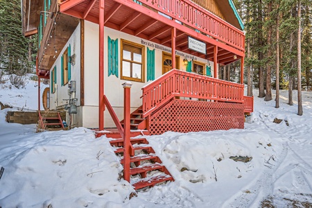 Two-story building in a snowy landscape, with red railings, teal window shutters, and a sign reading "Fine Pastries" above the porch. A set of red stairs leads up to the wooden porch.