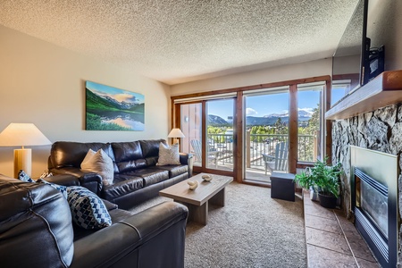 Cozy up in this inviting living room with plush leather seating, a warm stone fireplace, and stunning mountain views right from your private balcony.