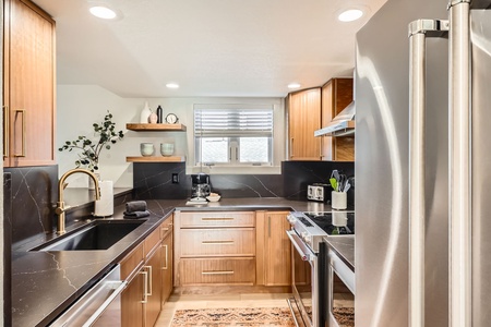 Fully equipped kitchen with sleek black quartz countertops, stainless steel appliances, and warm wood cabinetry — perfect for preparing meals or a morning coffee before hitting the slopes.