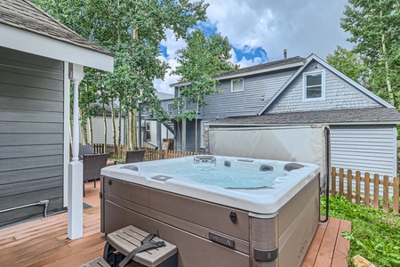 A wooden deck featuring a hot tub, outdoor furniture, and surrounding greenery with a two-story house in the background.