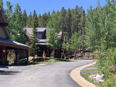 A quiet residential street with houses surrounded by trees and a clear blue sky. There is a fire hydrant and a shed visible in the background.