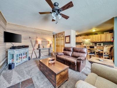 Inviting living room featuring comfortable seating, a flat-screen TV, a ceiling fan, and a cozy fireplace.