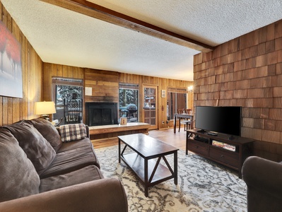 View of the inviting living room featuring comfortable seating, a 55” smart TV, DVD player, and a cozy wood-burning fireplace