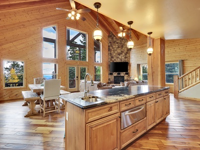 View of Kitchen Island and Great Room, with vaulted ceilings, floor to ceiling windows with expansive views of the mountains, comfortable seating, stone gas fireplace and flat screen TV