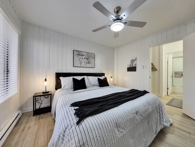 View of primary bedroom with plush bedding and king size bed, two night stands with laps, ceiling fan, armoire, space heater, and private use stacked washer and dryer.