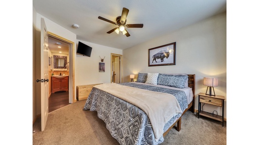 Spacious primary bedroom featuring a king-size bed, ceiling fan for comfort, 32" TV, and an attached bathroom for added convenience