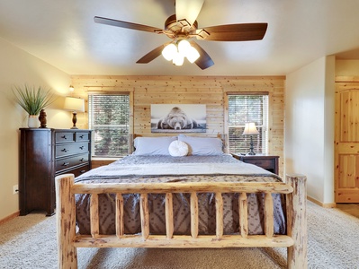 View of Primary Bedroom located on the ground level, with king size bed, ceiling fan, gas fire place, plush bedding and attached bathroom