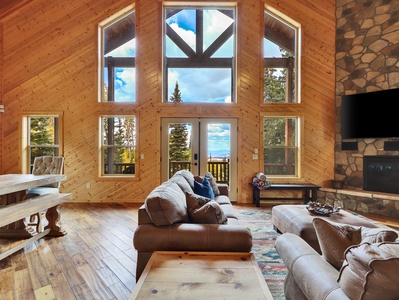 View of the Great Room, with vaulted ceilings, floor to ceiling windows with expansive views of the mountains, comfortable seating, stone gas fireplace and flat screen TV