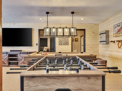 Game room equipped with a foosball table, pool table, entertainment center featuring a 72" TV and soundbar, a stone fireplace, and a comfortable sectional sofa.