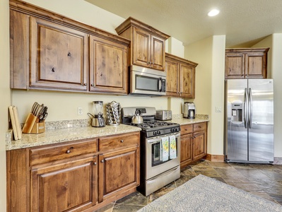 View of fully equipped kitchen featuring a coffee maker, microwave, stove/oven, upgraded cabinetry, granite countertops, blender, kettle, cooking spices, and stainless steel refrigerator