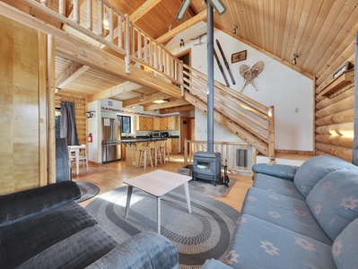 Open-concept view of the living room, loft, and kitchen, centered around a cozy wood-burning stove.