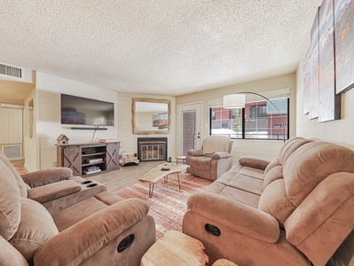 Cozy living space featuring a wood-burning fireplace, custom mirror, comfortable sofa and armchair, floor lamp, coffee table, media console, and a 53" smart TV—perfect for relaxing after a day in the mountains
