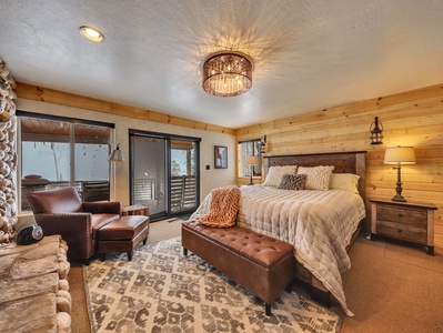 Primary bedroom with an en suite bathroom, a king-size bed, a wood-burning stone fireplace, and a private full-length sliding glass door leading to a covered veranda