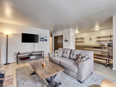 View of the light and airy living room with comfortable sofa, coffee table, wood burning fire place and 48" Smart TV