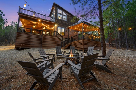 Outdoor firepit with adirondack chairs, string lighting and the back of the Counting Stars cabin in the background.